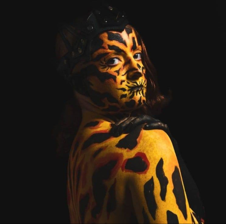 Person with tiger face paint and body paint against a black background
